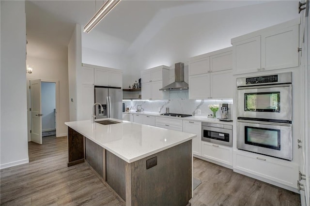 kitchen with wall chimney range hood, sink, appliances with stainless steel finishes, lofted ceiling, and a center island with sink