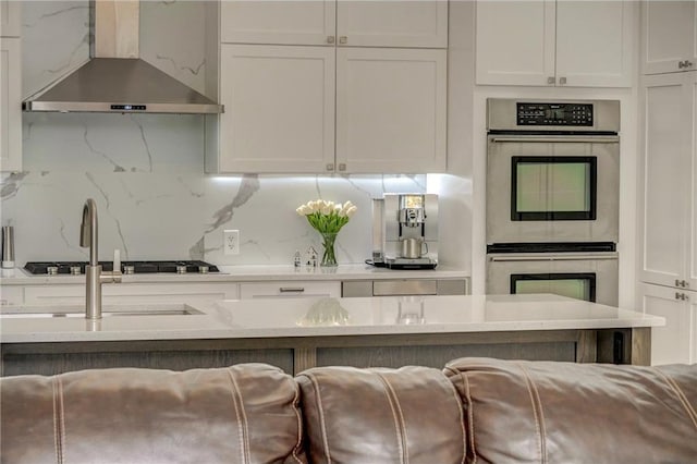 kitchen featuring wall chimney exhaust hood, white cabinetry, double oven, and tasteful backsplash