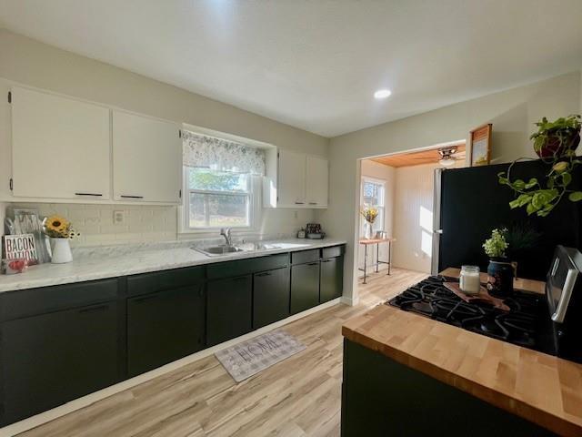 kitchen featuring white cabinetry, sink, black fridge, light hardwood / wood-style floors, and decorative backsplash