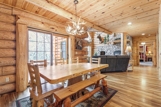 dining space featuring a stone fireplace, wooden ceiling, light hardwood / wood-style flooring, and rustic walls