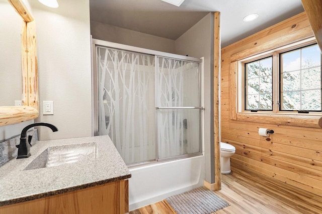 full bathroom featuring shower / bath combination with glass door, toilet, wooden walls, vanity, and hardwood / wood-style flooring