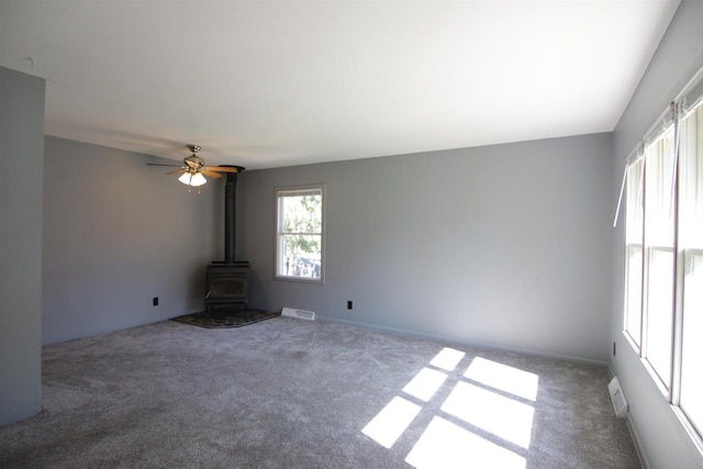 unfurnished living room with carpet floors, a wood stove, and ceiling fan