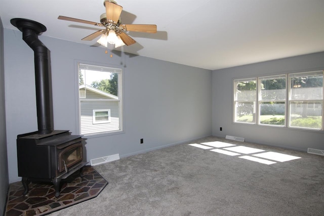 unfurnished living room featuring carpet, a wood stove, and ceiling fan