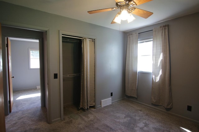 unfurnished bedroom with a closet, ceiling fan, multiple windows, and dark carpet