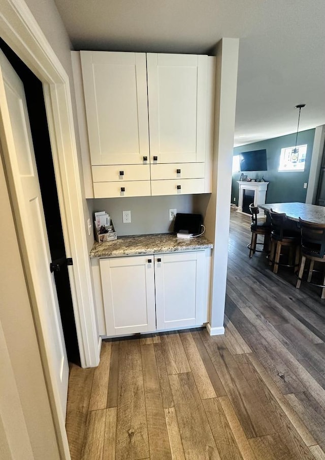 kitchen with white cabinetry, light stone counters, pendant lighting, and hardwood / wood-style floors