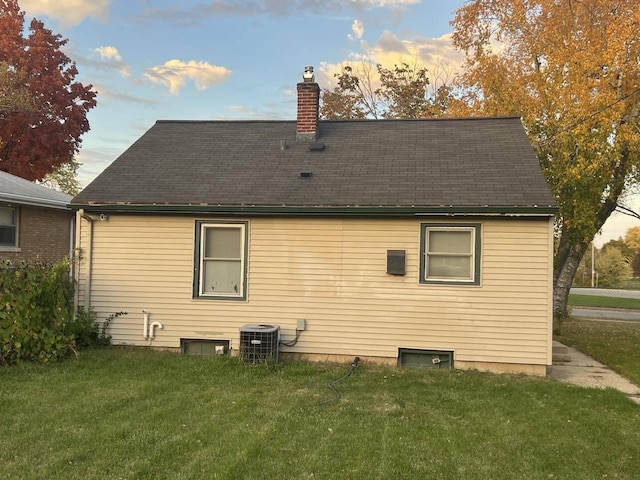 back house at dusk with central AC and a lawn