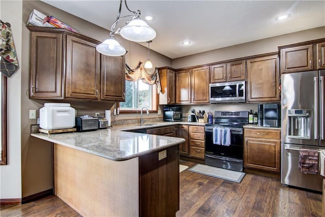 kitchen featuring dark wood-type flooring, stainless steel appliances, decorative light fixtures, and kitchen peninsula