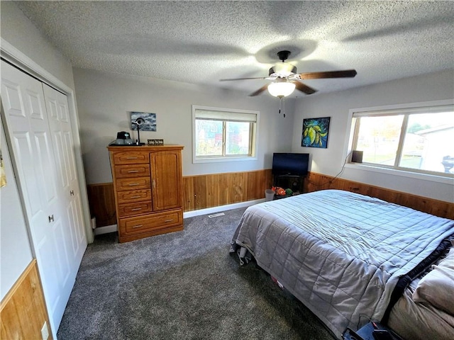 carpeted bedroom featuring a closet, ceiling fan, a textured ceiling, and wooden walls