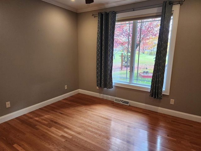 empty room with ornamental molding, ceiling fan, wood-type flooring, and a wealth of natural light