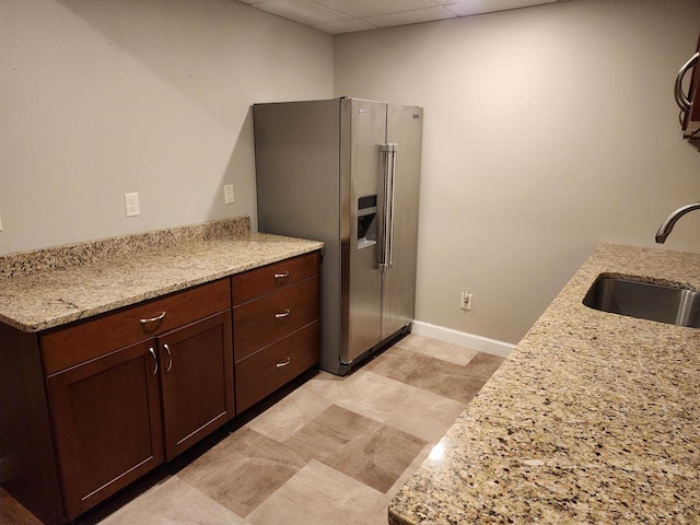 kitchen with dark brown cabinets, light stone counters, a paneled ceiling, high quality fridge, and sink