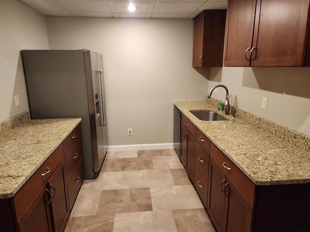 kitchen with stainless steel appliances, sink, a drop ceiling, dark brown cabinetry, and light stone counters