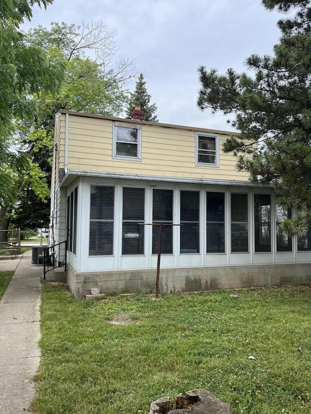 view of property exterior featuring a yard, central air condition unit, and a sunroom