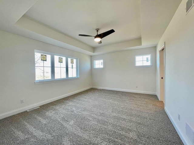 carpeted empty room featuring ceiling fan and a raised ceiling