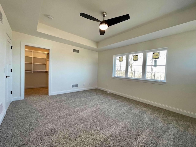 unfurnished bedroom with a closet, a spacious closet, ceiling fan, and a tray ceiling