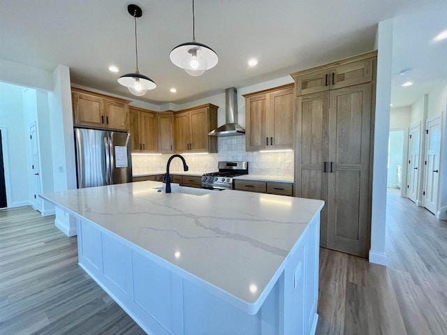 kitchen featuring appliances with stainless steel finishes, backsplash, light stone counters, a center island with sink, and wall chimney exhaust hood