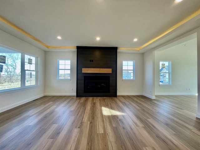 unfurnished living room featuring a large fireplace, plenty of natural light, a raised ceiling, and light hardwood / wood-style flooring