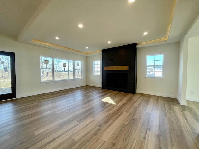 unfurnished living room with plenty of natural light, a large fireplace, light hardwood / wood-style floors, and a tray ceiling