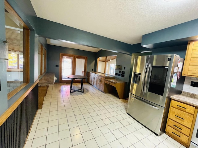 kitchen with stainless steel fridge, a textured ceiling, backsplash, and light tile patterned floors