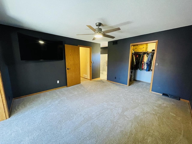 unfurnished bedroom featuring carpet, a walk in closet, a closet, and ceiling fan