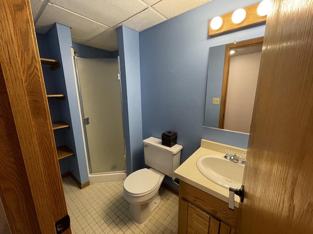 bathroom with a drop ceiling, a shower with shower door, toilet, vanity, and tile patterned flooring