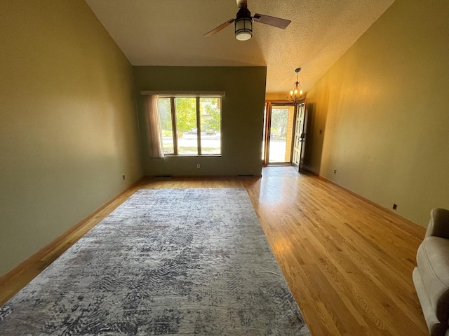 unfurnished room featuring light hardwood / wood-style floors, a textured ceiling, lofted ceiling, and ceiling fan with notable chandelier