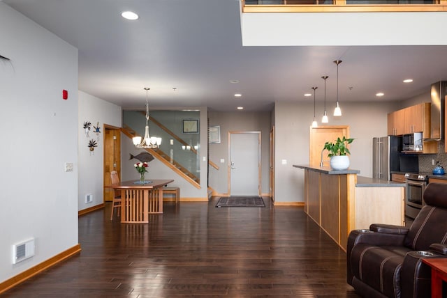 kitchen with appliances with stainless steel finishes, a notable chandelier, dark wood-type flooring, and pendant lighting