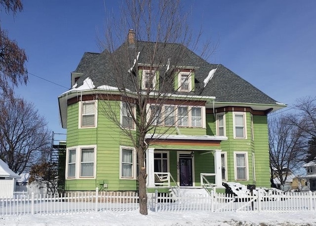 victorian house with stairway, a shingled roof, a porch, and a fenced front yard