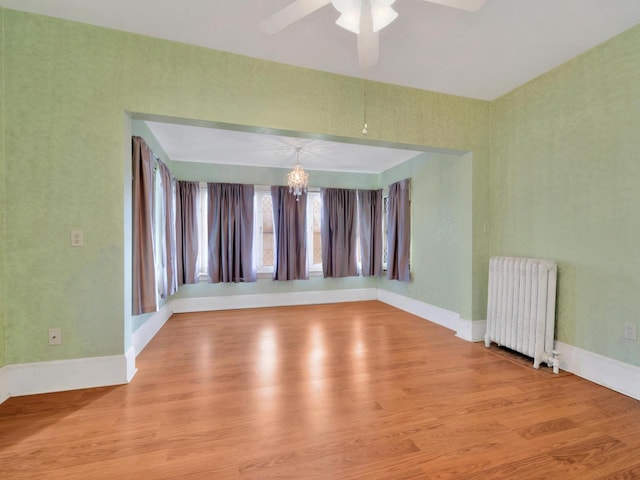 unfurnished room with radiator, wood finished floors, baseboards, and ceiling fan with notable chandelier