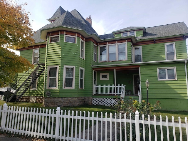 victorian-style house with a fenced front yard, a shingled roof, and covered porch