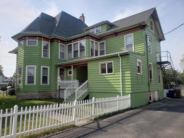 victorian house with roof with shingles, a chimney, covered porch, fence private yard, and stairs