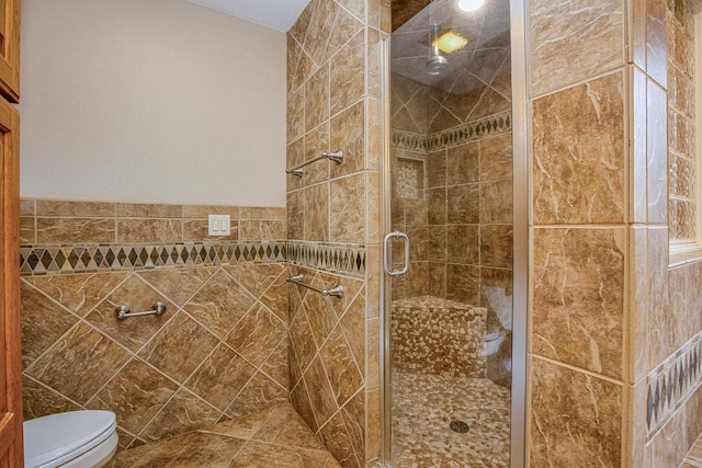 bathroom with toilet, tile walls, and a shower with shower door