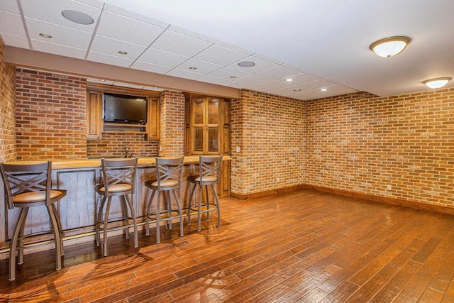 bar with a drop ceiling, hardwood / wood-style flooring, and brick wall