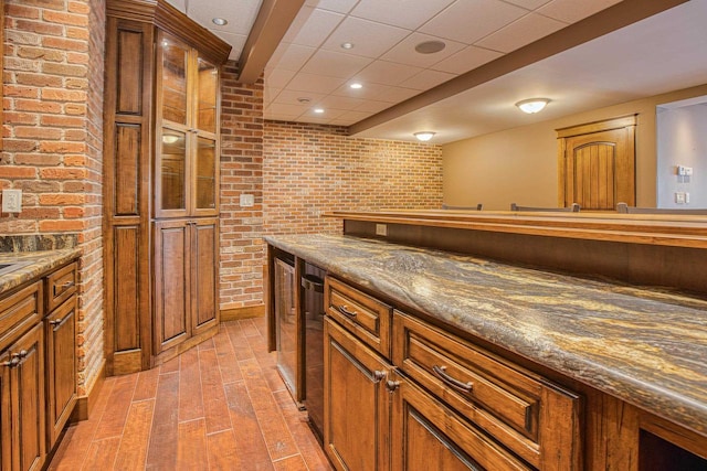 bar featuring brick wall, light hardwood / wood-style floors, and dark stone countertops