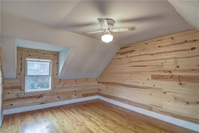 bonus room with light hardwood / wood-style flooring, wood walls, lofted ceiling, and ceiling fan