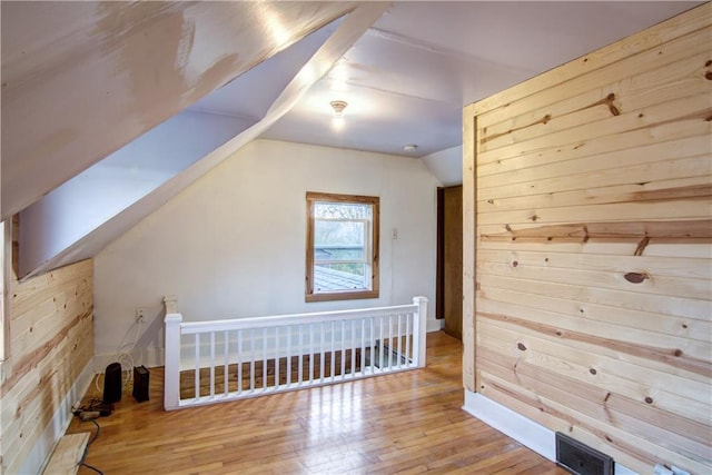 bonus room with lofted ceiling with skylight, light wood-type flooring, and wooden walls