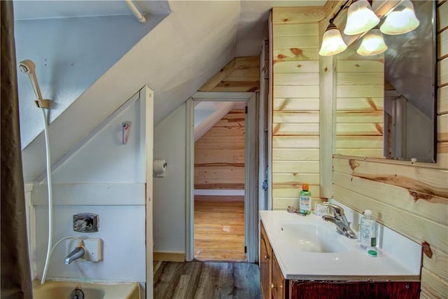 bathroom featuring lofted ceiling, hardwood / wood-style flooring, a washtub, vanity, and wood walls