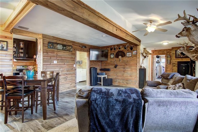 living room featuring hardwood / wood-style flooring, washer / clothes dryer, beam ceiling, wooden walls, and ceiling fan