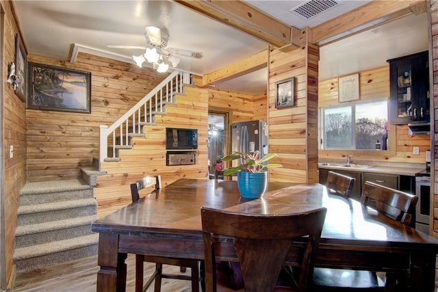 dining area featuring light hardwood / wood-style flooring, wood walls, beam ceiling, and ceiling fan