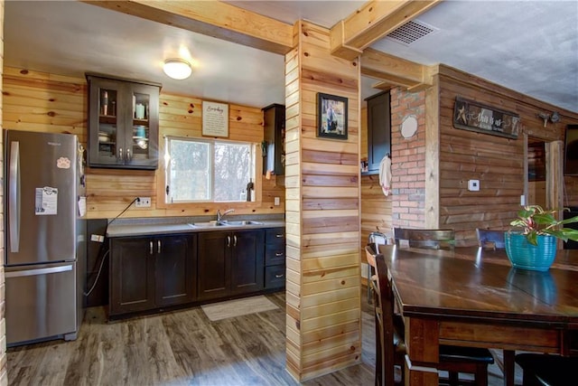 kitchen with sink, wooden walls, wood-type flooring, and stainless steel refrigerator