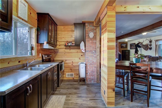 kitchen with wooden walls, stainless steel electric stove, dark brown cabinets, sink, and dark hardwood / wood-style flooring