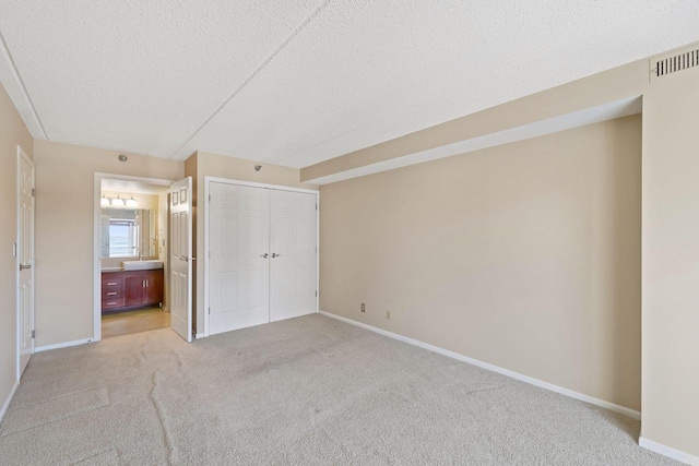 unfurnished bedroom with ensuite bath, light carpet, a closet, and a textured ceiling