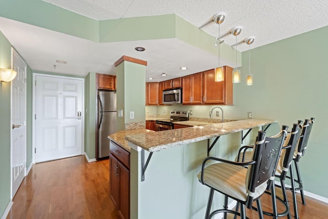 kitchen featuring kitchen peninsula, a textured ceiling, stainless steel appliances, wood-type flooring, and pendant lighting