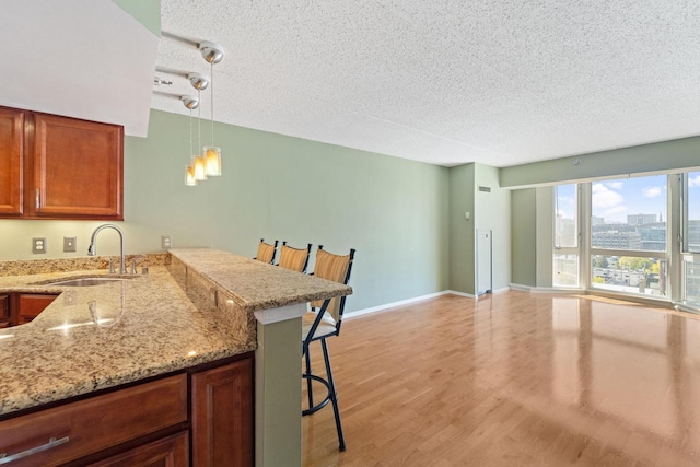 kitchen featuring a kitchen breakfast bar, sink, light hardwood / wood-style floors, light stone counters, and kitchen peninsula