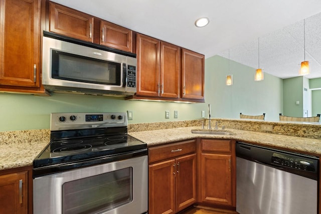 kitchen featuring light stone counters, a textured ceiling, stainless steel appliances, sink, and decorative light fixtures