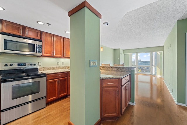 kitchen featuring light stone countertops, a textured ceiling, stainless steel appliances, and light hardwood / wood-style flooring