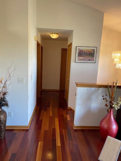 corridor with an inviting chandelier, lofted ceiling, and dark hardwood / wood-style flooring