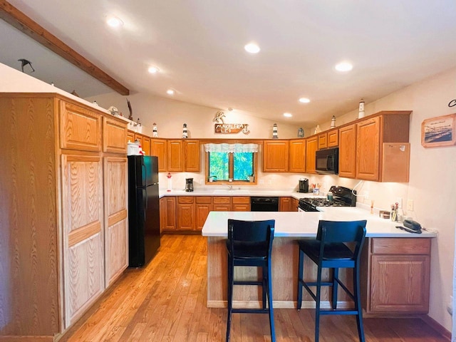 kitchen with kitchen peninsula, black appliances, lofted ceiling with beams, a breakfast bar, and light hardwood / wood-style floors