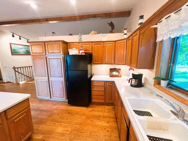 kitchen featuring beam ceiling, sink, light wood-type flooring, and black fridge