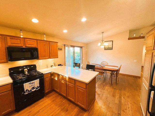 kitchen featuring kitchen peninsula, light wood-type flooring, vaulted ceiling, black appliances, and pendant lighting