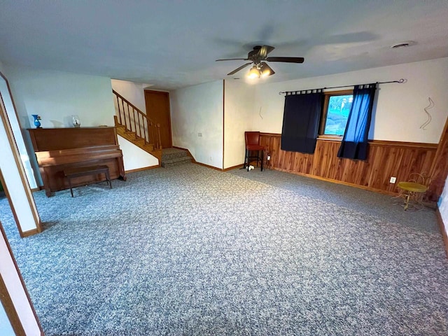 carpeted empty room with wood walls and ceiling fan